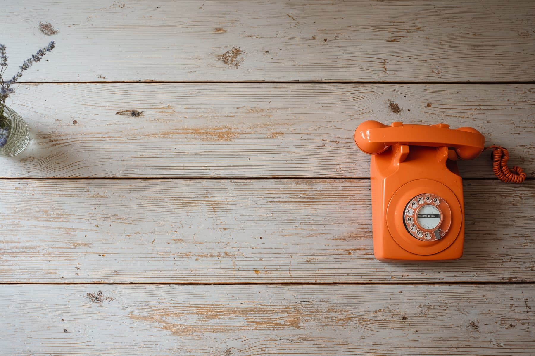 An orange rotary phone and a jar of lavender on a whitewashed wooden table